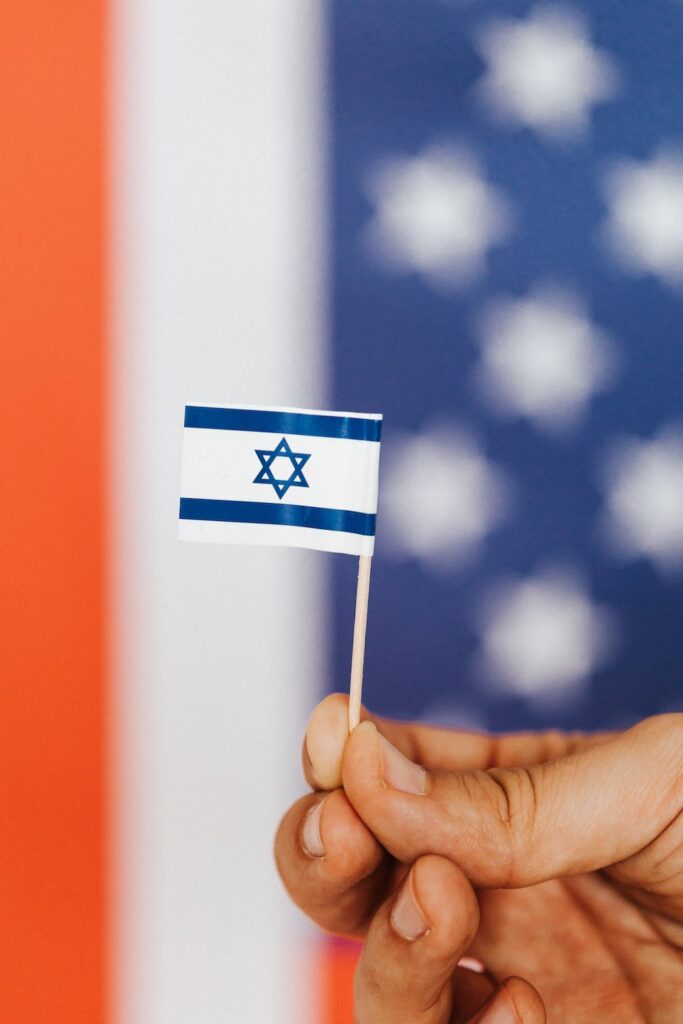Someone holding a mini Israeli flag in front of the star spangled banner.